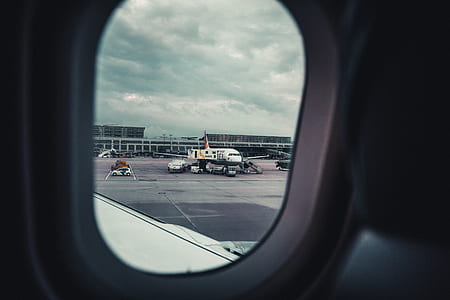 aircraft window view of white airplane on runway under white cloudy skies at daytime thumbnail