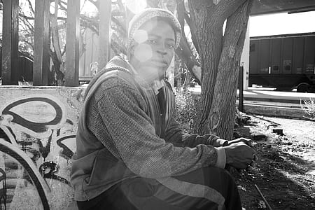 grayscale photo of a man sitting nearby tree thumbnail