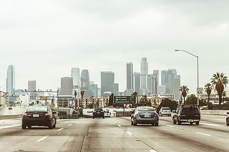 vehicles on gray road near building under white sky thumbnail