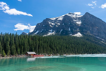 snow covered mountain with surrounding pine trees and body of water during daytime thumbnail