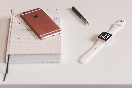 Silver Apple Watch White Sports Band Near Rose Gold Iphone 6 on White Wooden Table thumbnail