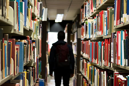 man in black jacket standing at the isle of bookshelves thumbnail