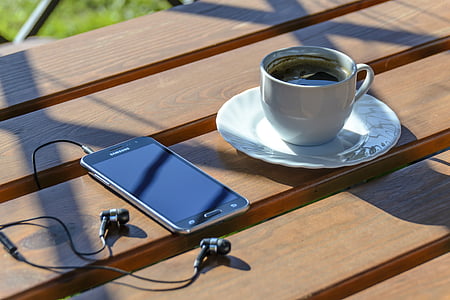 black Samsung Android smartphone with turned-off screen beside cup of coffee on top of brown wooden surface thumbnail
