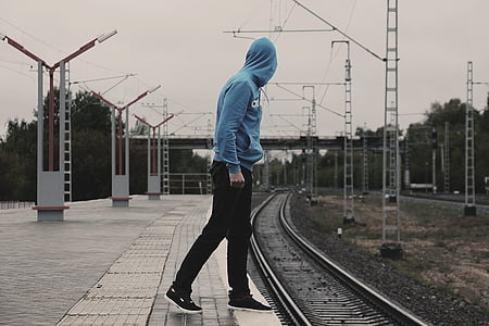 man wearing blue pullover hoodie walking on railroad photography during daytime thumbnail