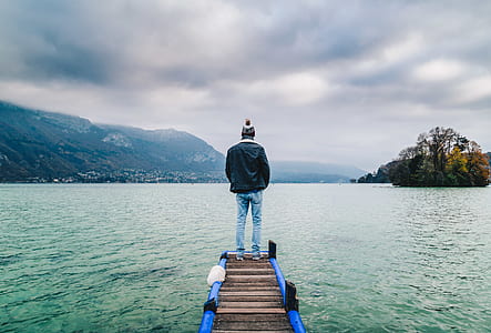 man standing on dock facing body of water thumbnail