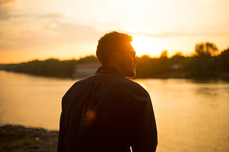 man wearing sunglasses in front of calm body of water during golden hour thumbnail