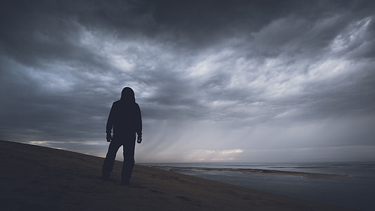 silhouette photography of person standing on sand facing sea thumbnail