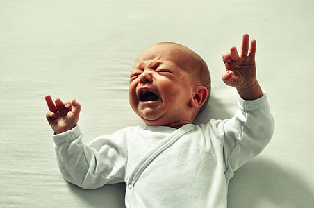 baby in white clothes crying while lying on white cushion thumbnail