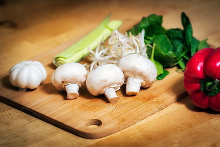 food photography of red bell pepper beside brown chopping board with three white mushrooms and one garlic bulb thumbnail