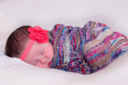 baby sleeping wearing multicolored blanket and red flower headband in closeup photography thumbnail