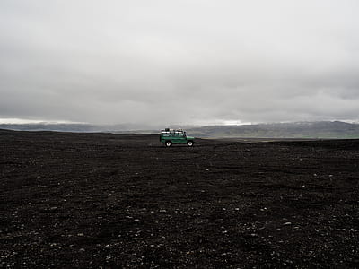 green SUV on open field in distant of mountain under nimbus clouds thumbnail