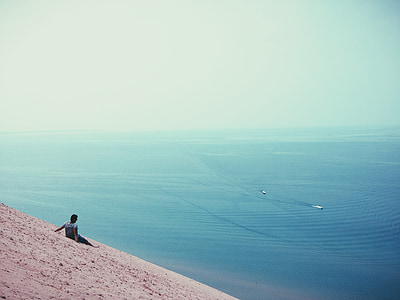 person sitting on beach sand facing body of water thumbnail