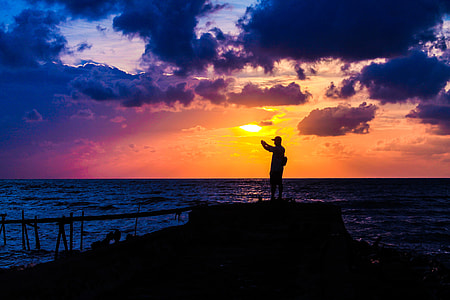 silhouette photo of person standing near ocean during sunset thumbnail