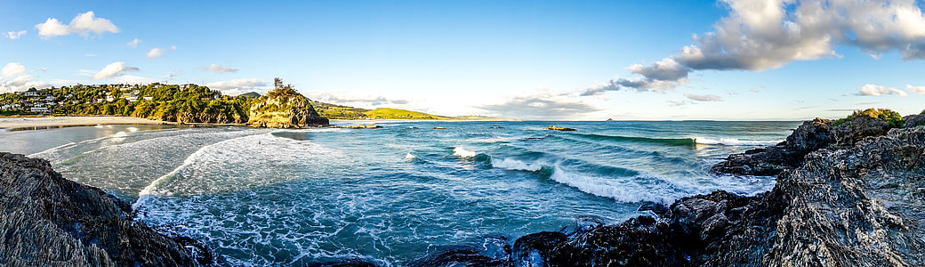 sea near green mountain under blue and white cloudy sky thumbnail