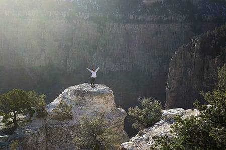 Woman in White Coat and Black Pants Standing on Brown Rock Formation Mountain thumbnail