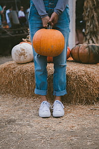 person standing while holding pumpkin near hay thumbnail