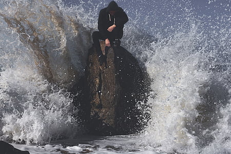 man in black hoodie sitting on coastal rock during daytime thumbnail