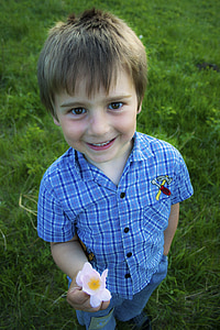 boy holding flower while standing on grass field thumbnail