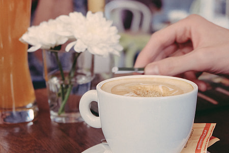 white ceramic teacup filled with brown liquid placed near white petaled flower centerpiece on beige wooden table thumbnail