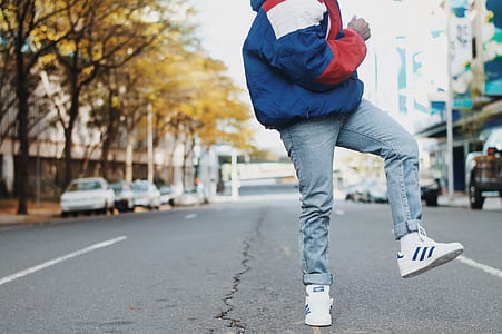 person wearing jacket and jeans standing on concrete road near cars thumbnail