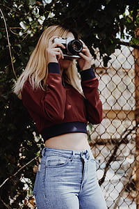 woman taking photo using gray and black camera near black chain link fence at daytime thumbnail