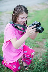 Shallow Focus Photo of a Girl in Pink Round-neck Shirt Holding Black Dslr Camera thumbnail