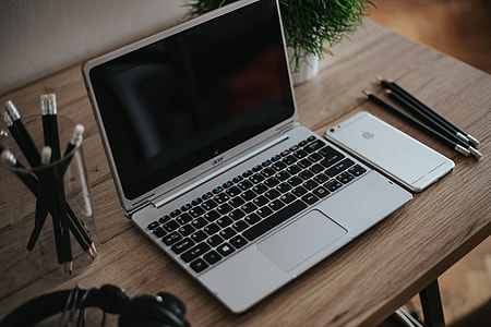 Silver Acer laptop on a wooden desk with a green plant, pencils and an Apple iPhone thumbnail