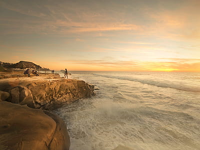 silhouette of person on brown cliff beside ocean during sunset thumbnail