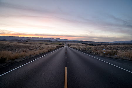 asphalt road in between grass field during daytime thumbnail