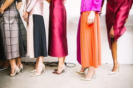 five women wearing assorted-color dresses and heeled shoes while standing near white wall thumbnail