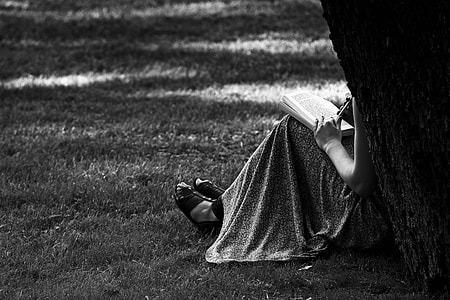 grayscale photo of person wearing dress and sandals leaning on tree thumbnail