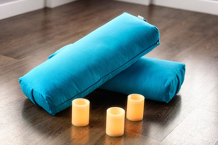 three white candles beside two blue pillows on brown surface thumbnail