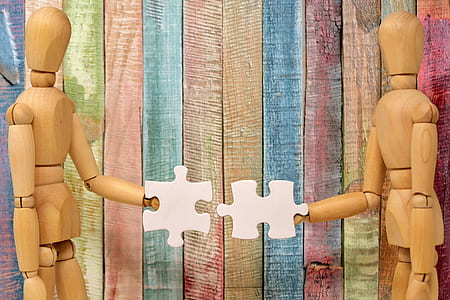 two wooden dummies holding two white puzzle pieces thumbnail