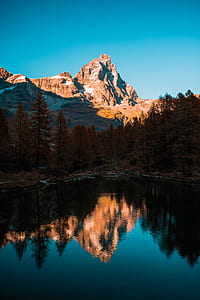 body of water surrounded by pine trees and mountain under blue skies thumbnail