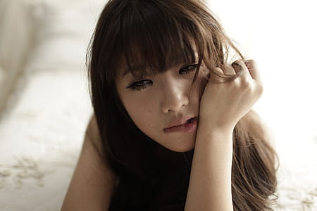 girl holding her face lying on white comforter thumbnail