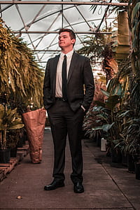 man in black suit jacket standing in middle of trees thumbnail