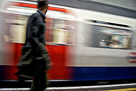 man standing beside blue and red train passing by thumbnail