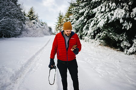 man in bubble jacket holding smartphone standing on snow field thumbnail
