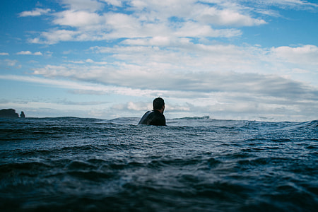 man wearing black top in ocean under white clouds and blue sky during daytime thumbnail