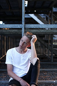 man wearing white shirt sitting on grass leaning on gray scaffolding thumbnail