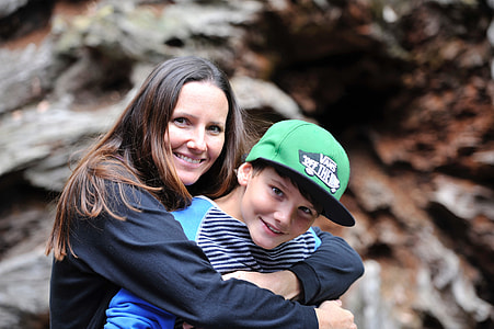 smiling woman wearing black long-sleeved top hugging boy wearing green snapback thumbnail