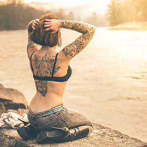 woman kneeling on stone in front of lake wearing black brassiere, jeans, and high-heeled boots during day thumbnail