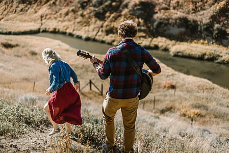 man holding guitar walking on green grass during daytime thumbnail