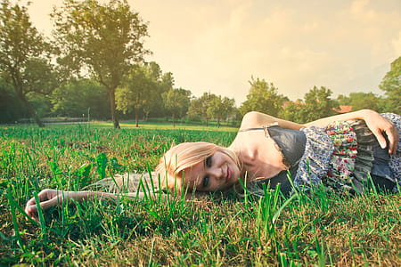 Young Blonde Woman In Spaghetti Straps Floral Skirt Lying On Grass In Sunlight thumbnail
