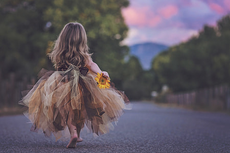 macro shot photography of girl in brown and black sleeveless gown holding sunflower during daytime thumbnail
