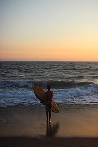person holding surfboard in front of body of water thumbnail