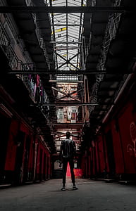 man standing on gray pavement inside gray and red building during daytime thumbnail
