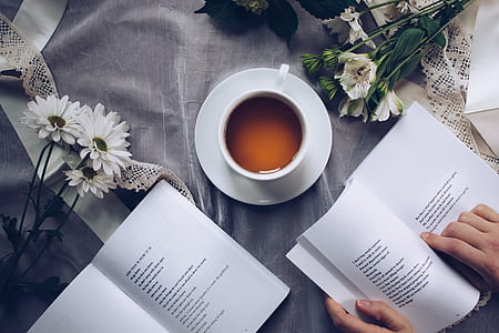 person placing book beside cup and saucer thumbnail