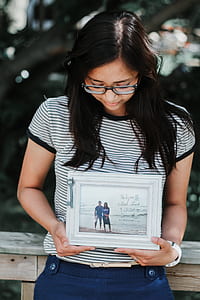 woman wearing eyeglasses holding white photo frame thumbnail
