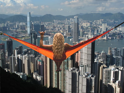 woman on orange swing above skyscrapers making a hangloose handsign at daytime thumbnail
